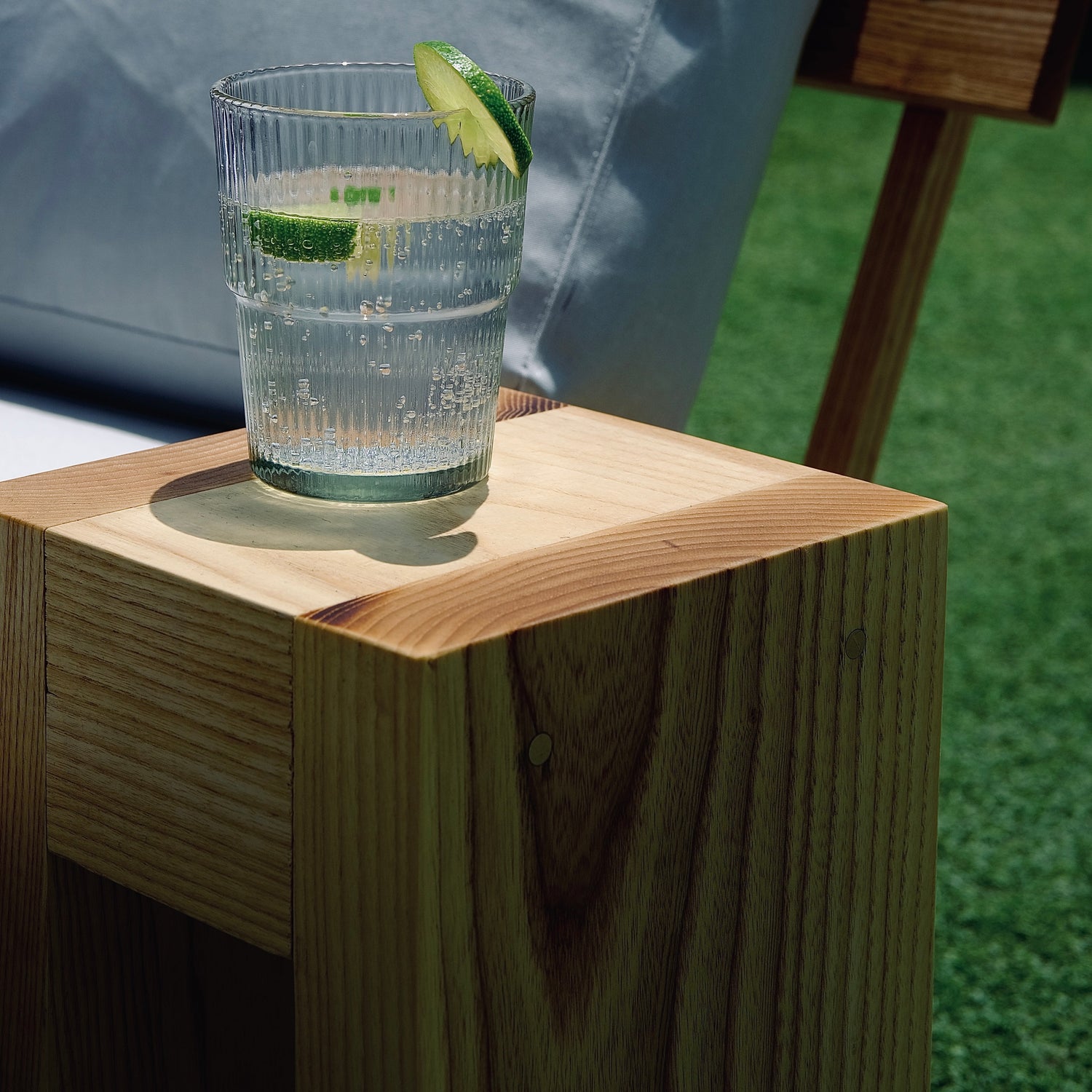 Glass of water with a lime wedge on a wooden drink table on grass