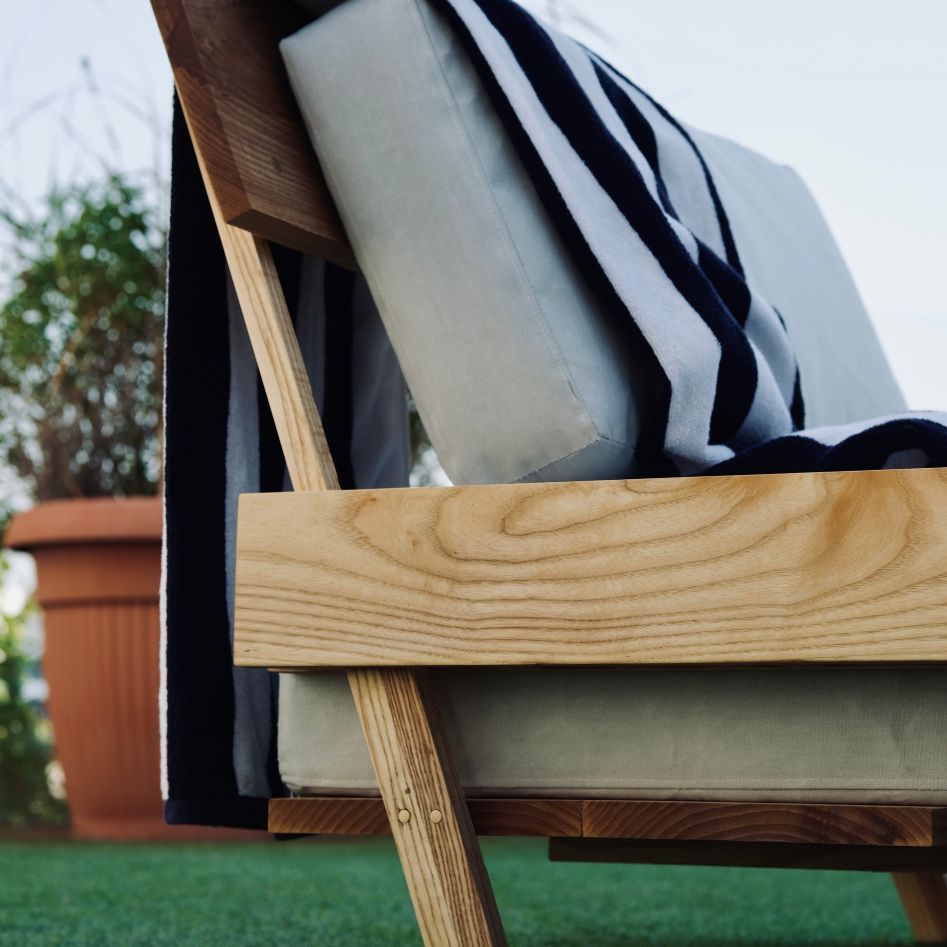 Wooden outdoor chair with a black and white striped towel draped over it on a grassy area.