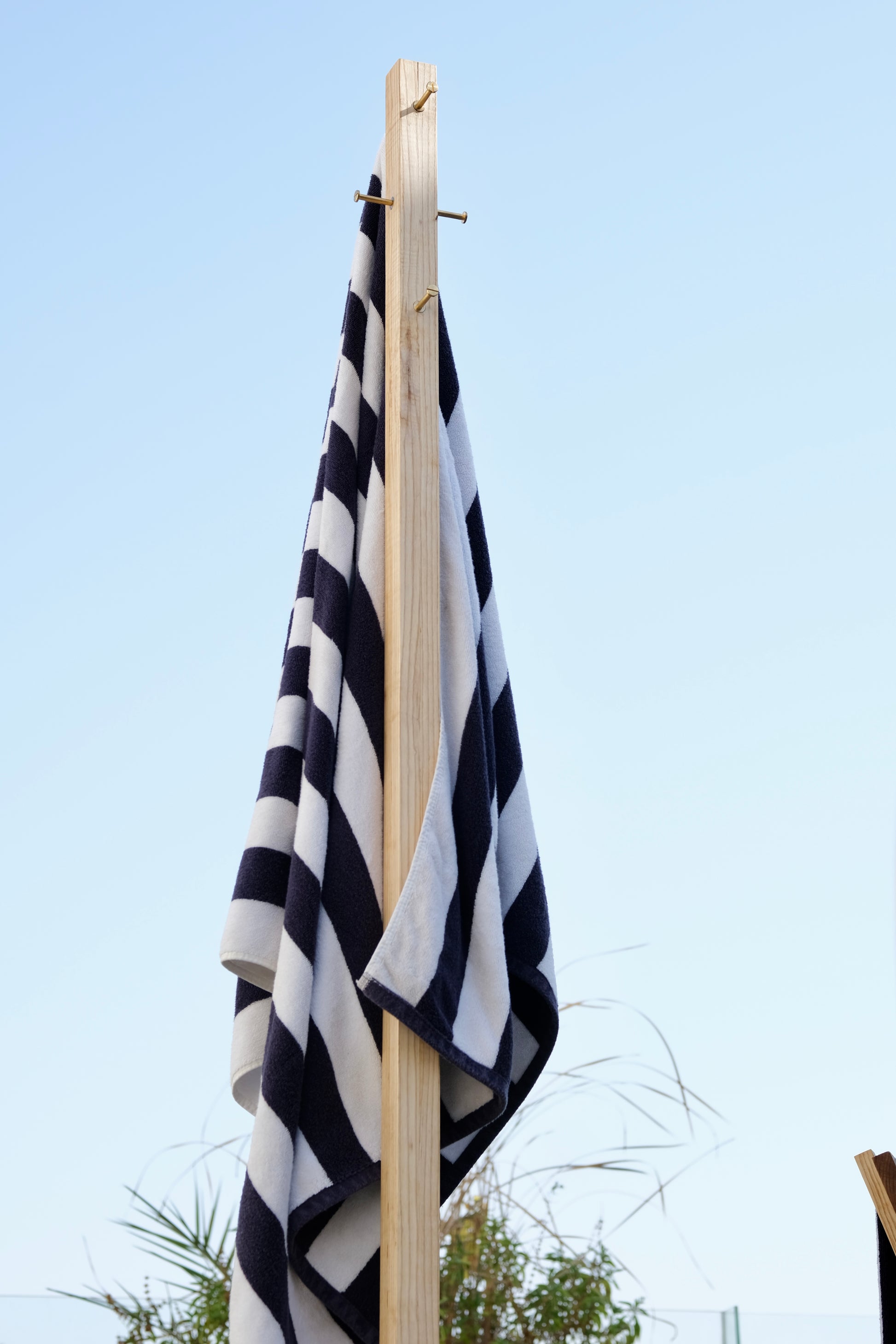 Black and white striped towel hanging on a wooden rack against a clear blue sky.