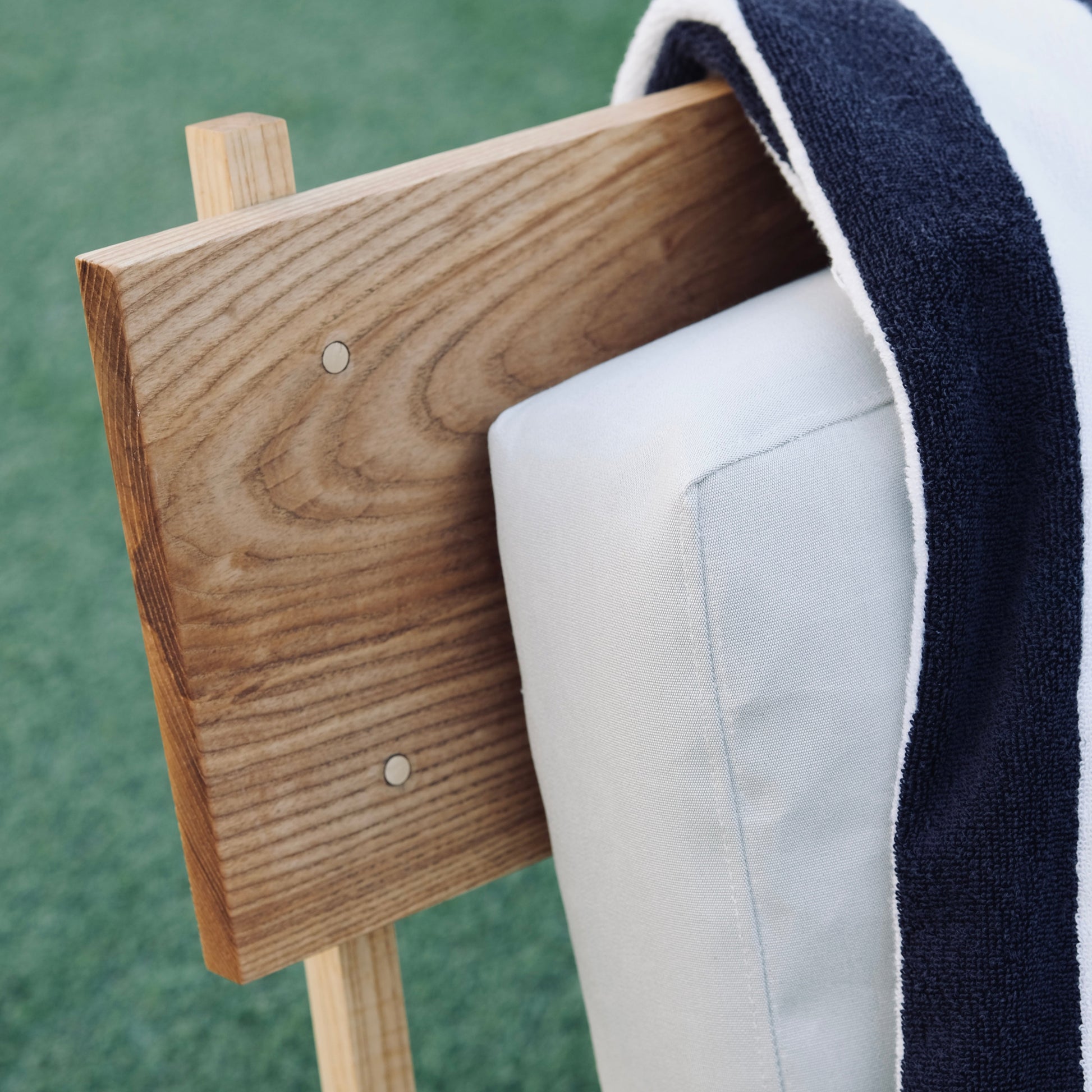 Wooden chair with a white cushion and a striped towel against a green background