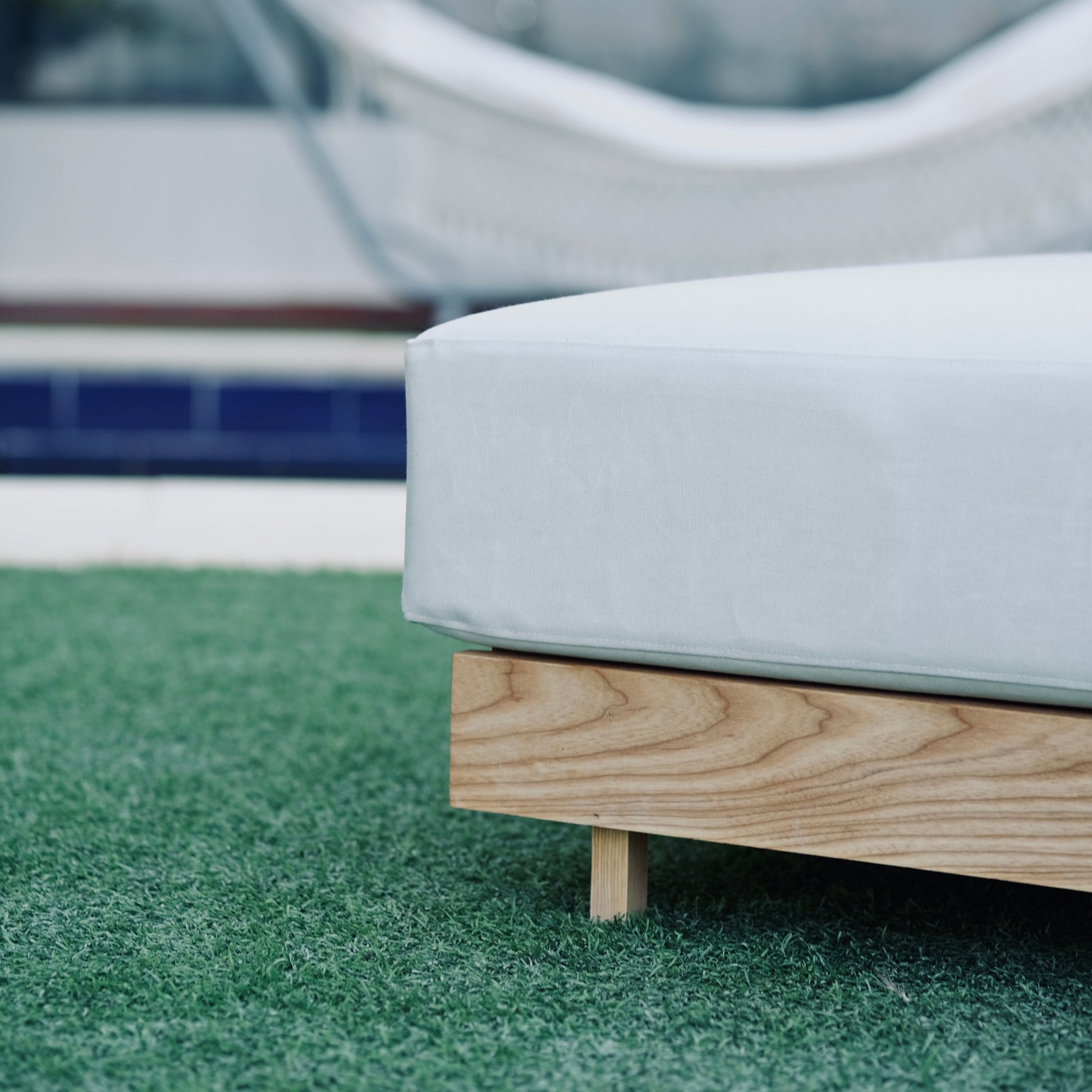 White outdoor ottoman with wooden legs on a grassy area