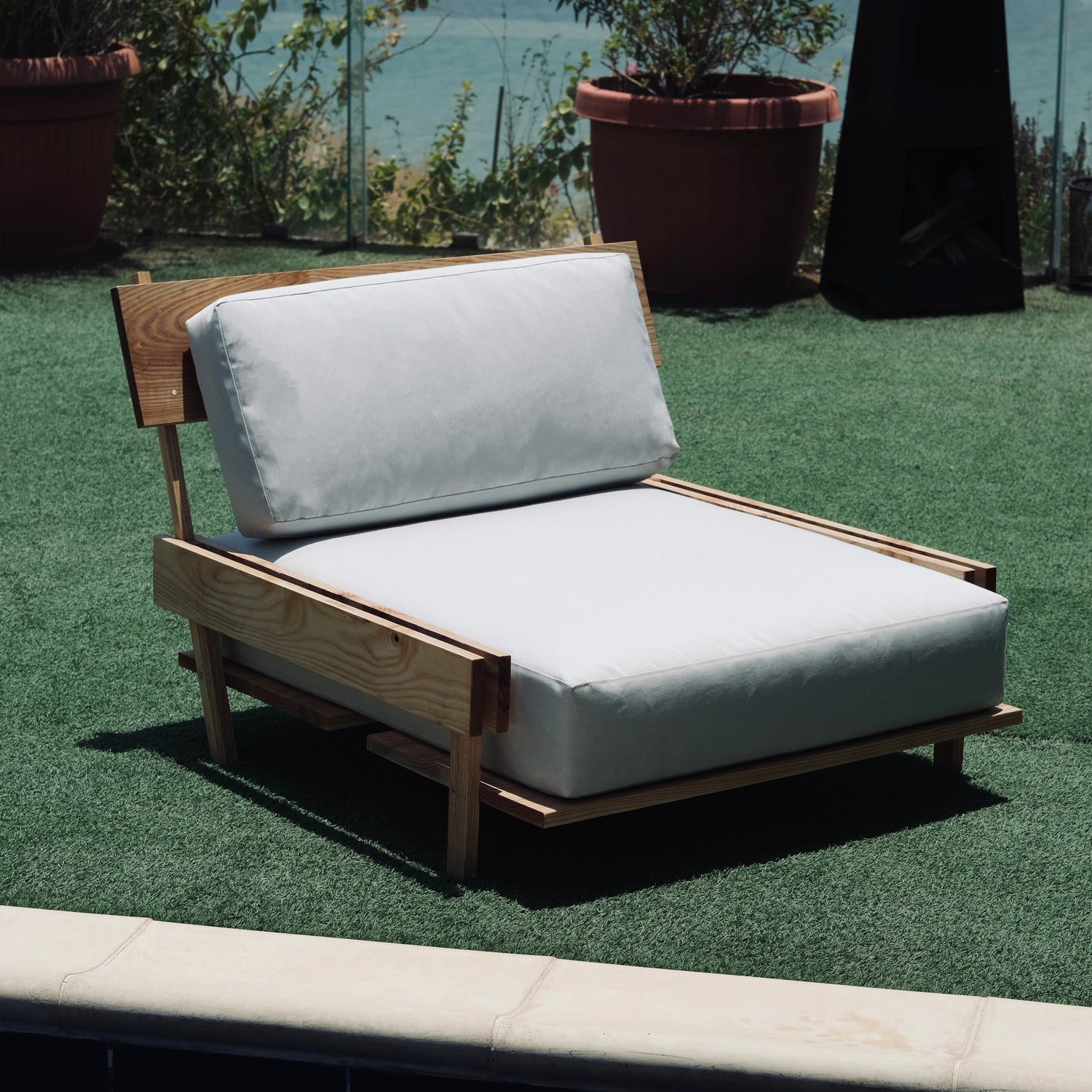 Wooden outdoor chair with white cushions on a grassy area.