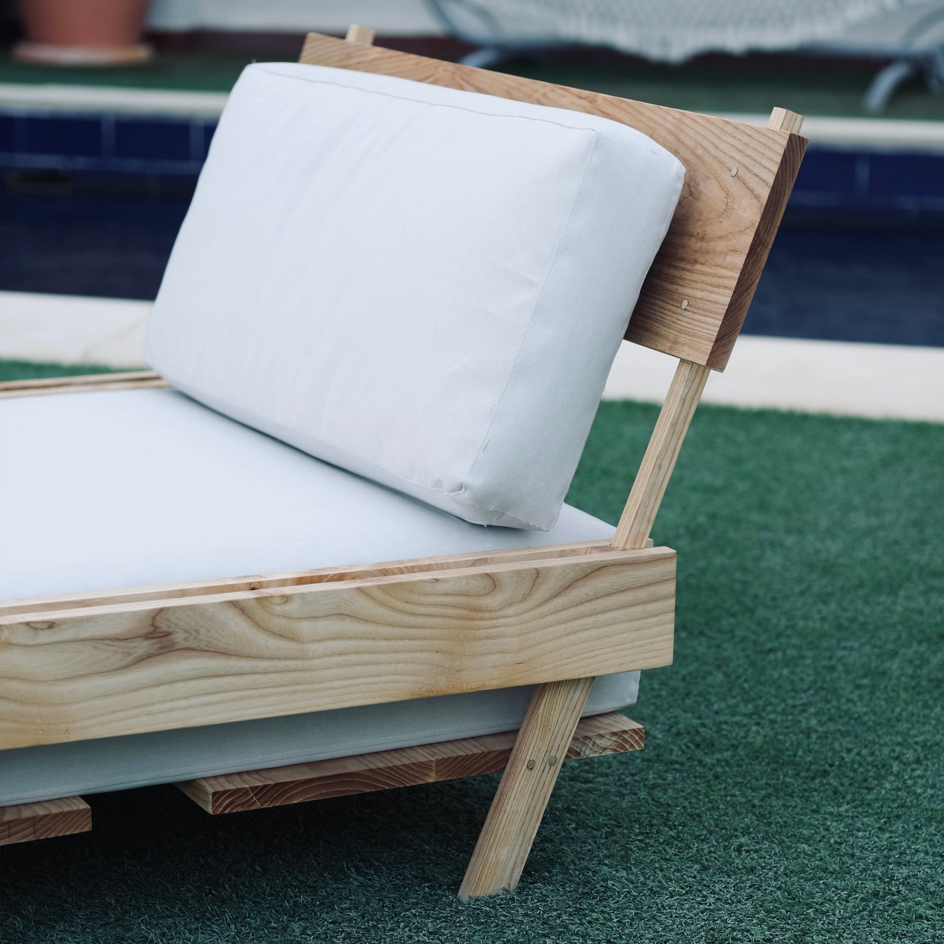 Wooden outdoor chair with white cushions on a green surface, near a pool.