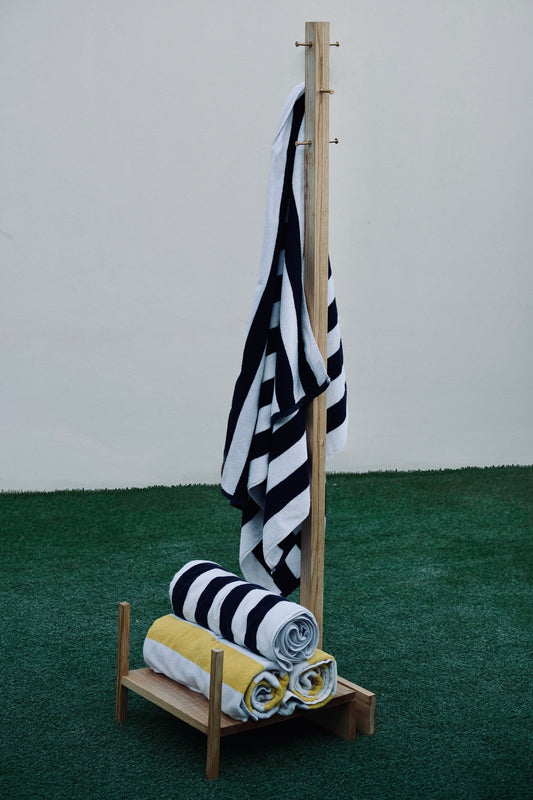 Black and white striped towel hanging on a wooden rack with a low shelf against a plain background